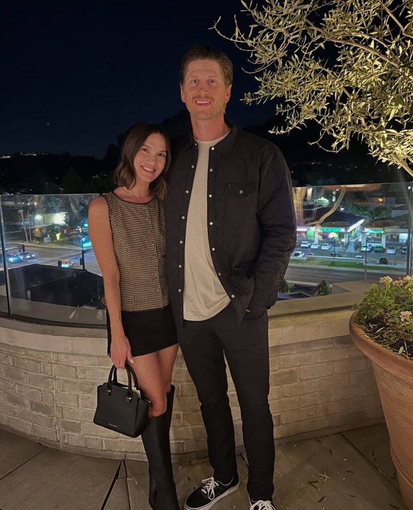 Couple posing outdoors at night wearing smart-casual dinner outfits for an anniversary.