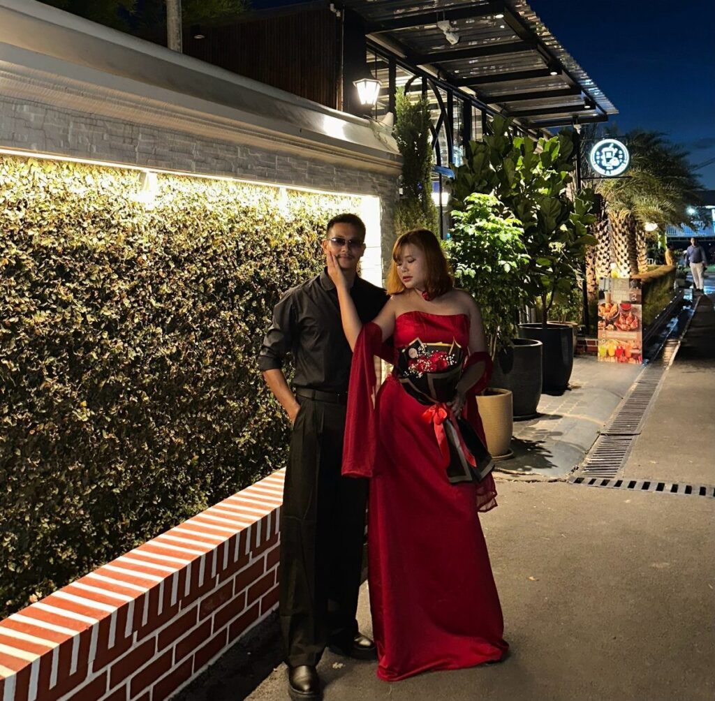 Woman in a long red evening gown and man in black posing outdoors.
