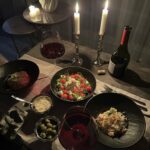 Candlelit dinner table with red wine, gourmet plates, and glowing white taper candles.
