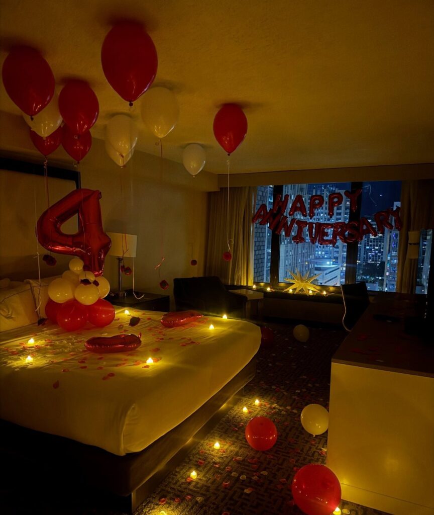 Red and white balloons and anniversary decorations in a dimly lit hotel room