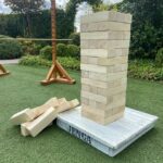 Giant wooden Jenga tower standing on a white base on green grass.