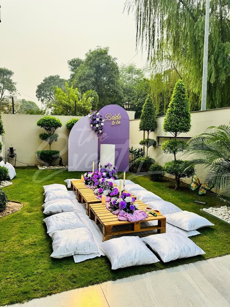 Low wooden pallet table with purple flowers and white cushions for bridal shower