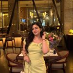 Woman in a light yellow summer dress holding a white handbag in a restaurant