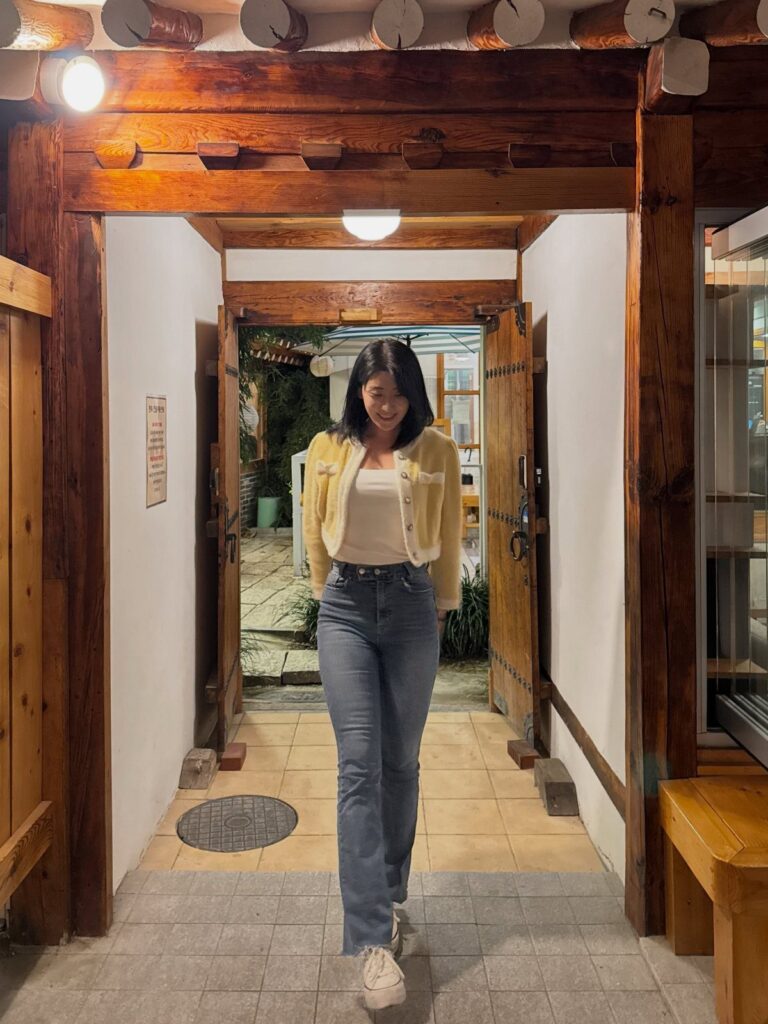 Woman wearing a yellow jacket and blue jeans standing in a rustic doorway