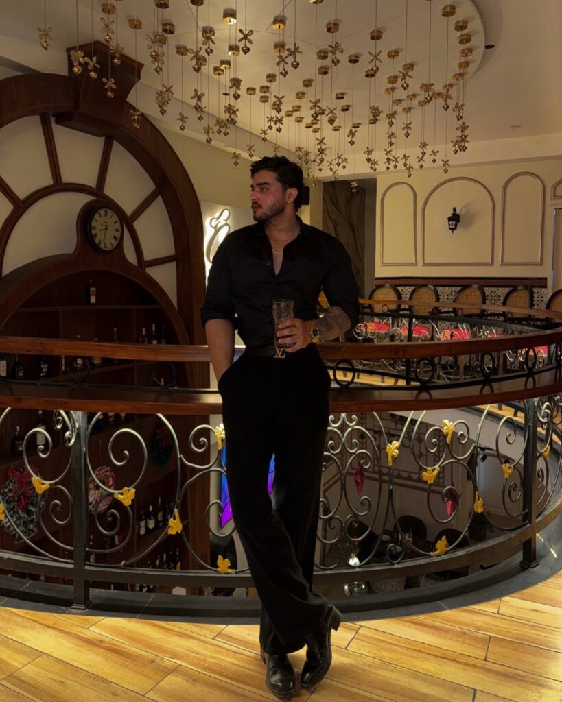 Man in all-black smart casual outfit posing by a railing in a restaurant
