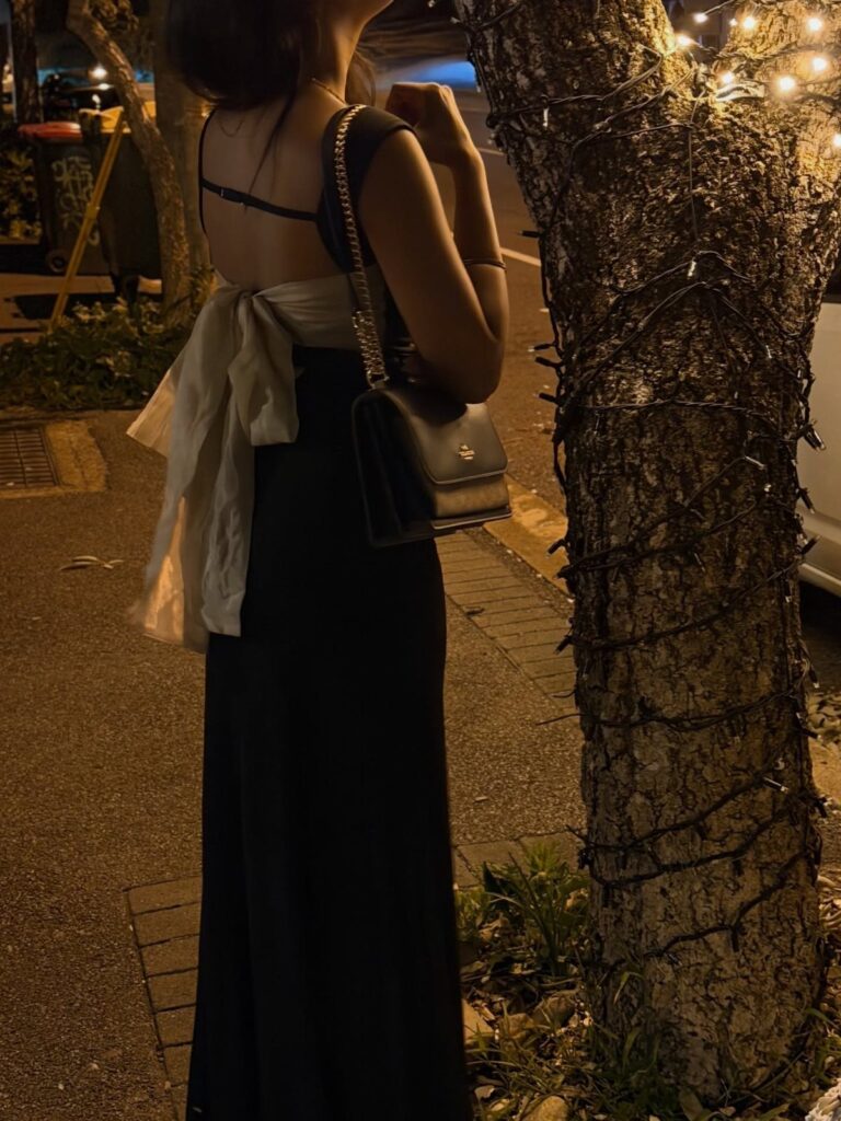 Woman in a long black dress with a white bow and black handbag.