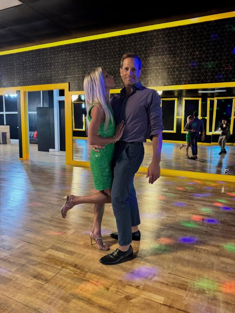 Couple posing in a dance studio with mirrors and colorful floor lights.