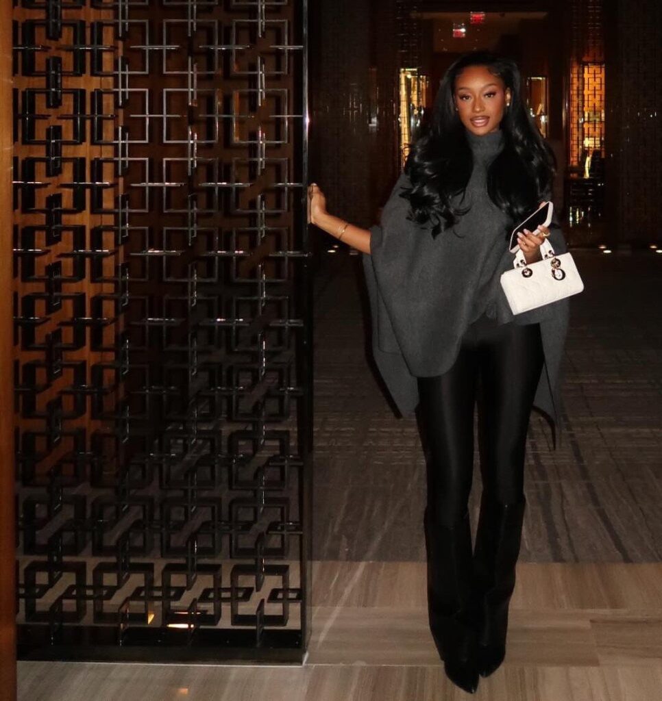 Woman wearing a grey oversized sweater, black leather leggings, and black heeled boots.