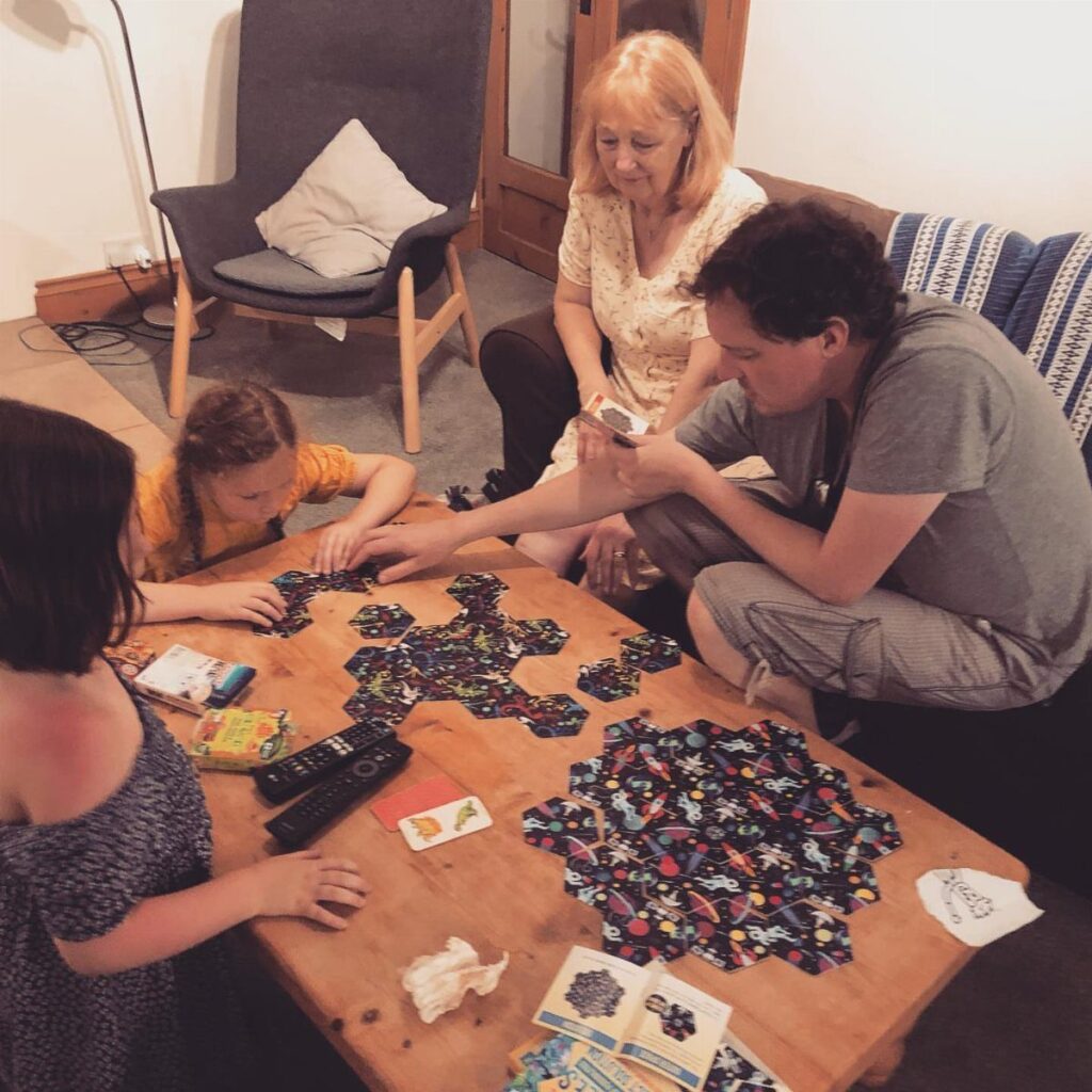Family playing a board game with hexagonal tiles on a wooden table.