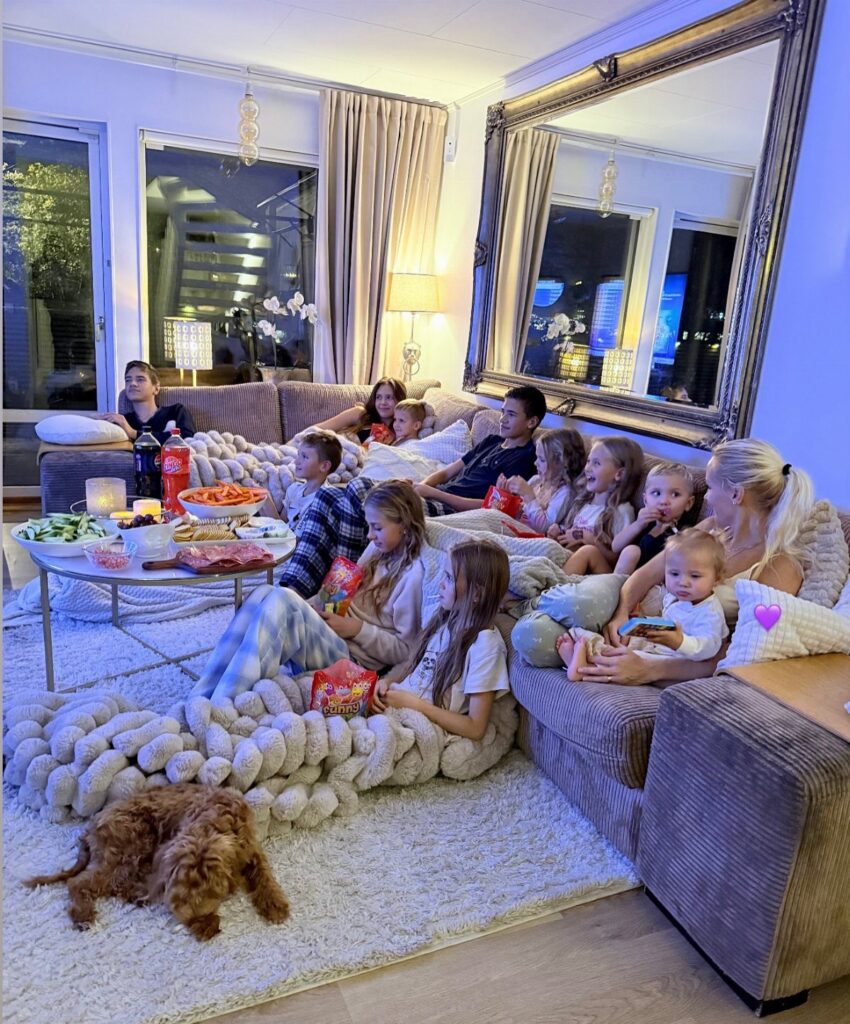 Family lounging on a sofa and rug with many blankets and pillows.