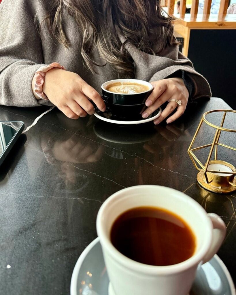 Two cups of coffee on a dark table with a person holding one.