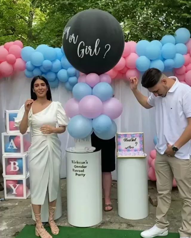 Couple standing before a pink and blue balloon arch for a gender reveal party.