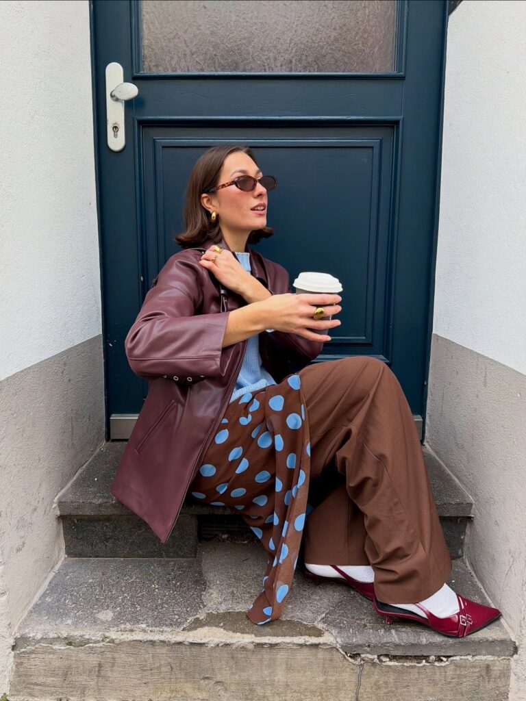 Woman in burgundy leather jacket and polka dot trousers sitting on stone steps.