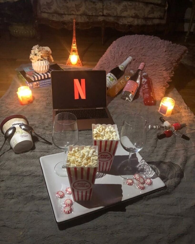 Netflix movie night setup with popcorn, wine glasses, and candles on a rug