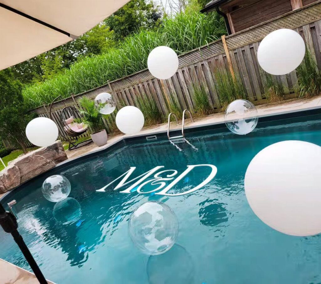Swimming pool decorated with floating white and clear balloons and white initials M&D.