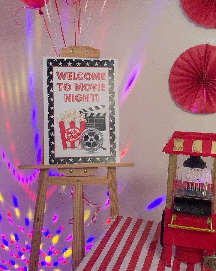 Movie night welcome sign on an easel next to a red popcorn machine.