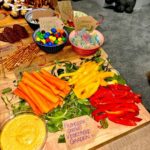 Assorted snacks including vegetable sticks, dip, and colorful candies on a wooden board.