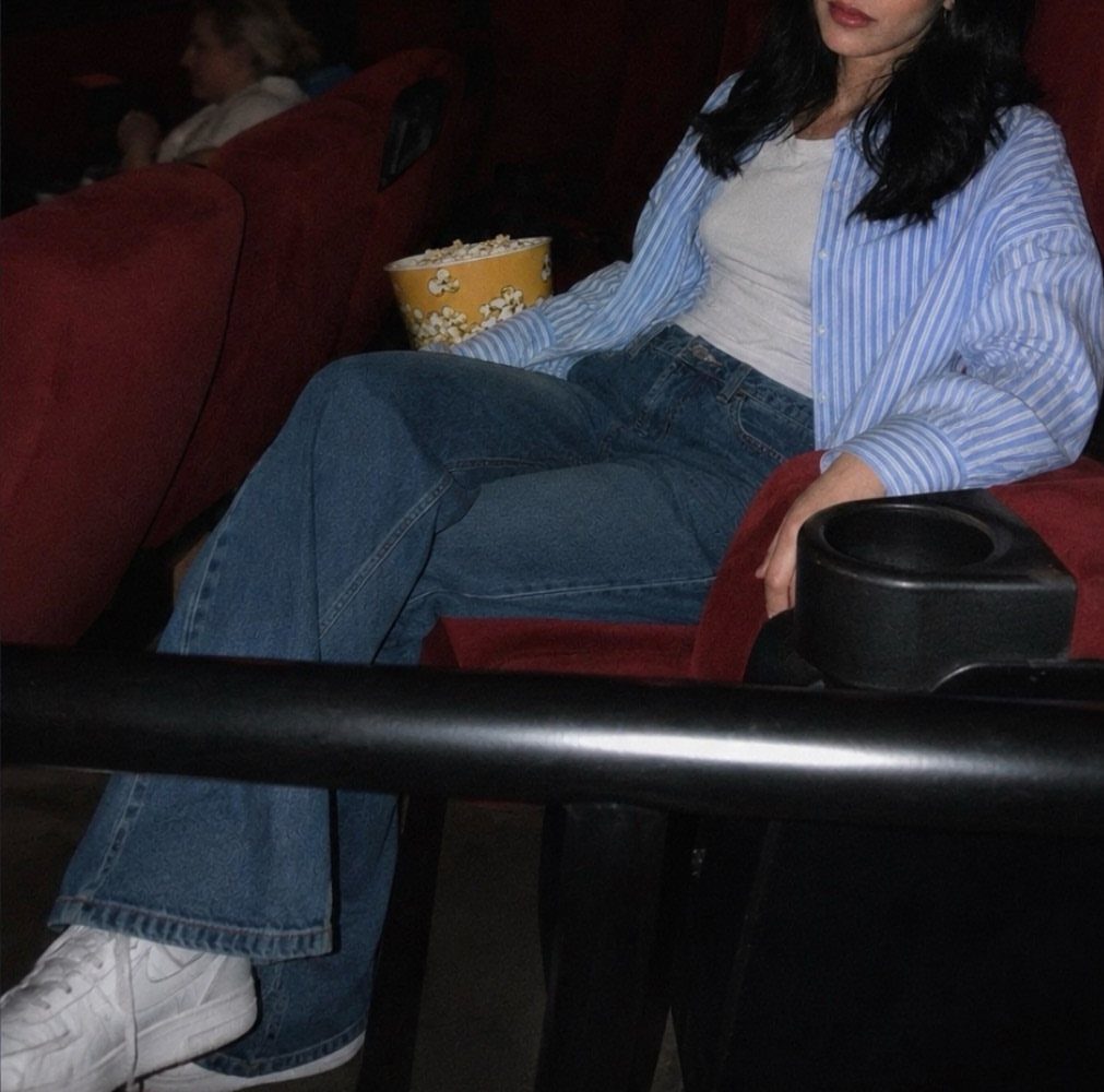 Person in a striped shirt and jeans sitting in a movie theater seat.