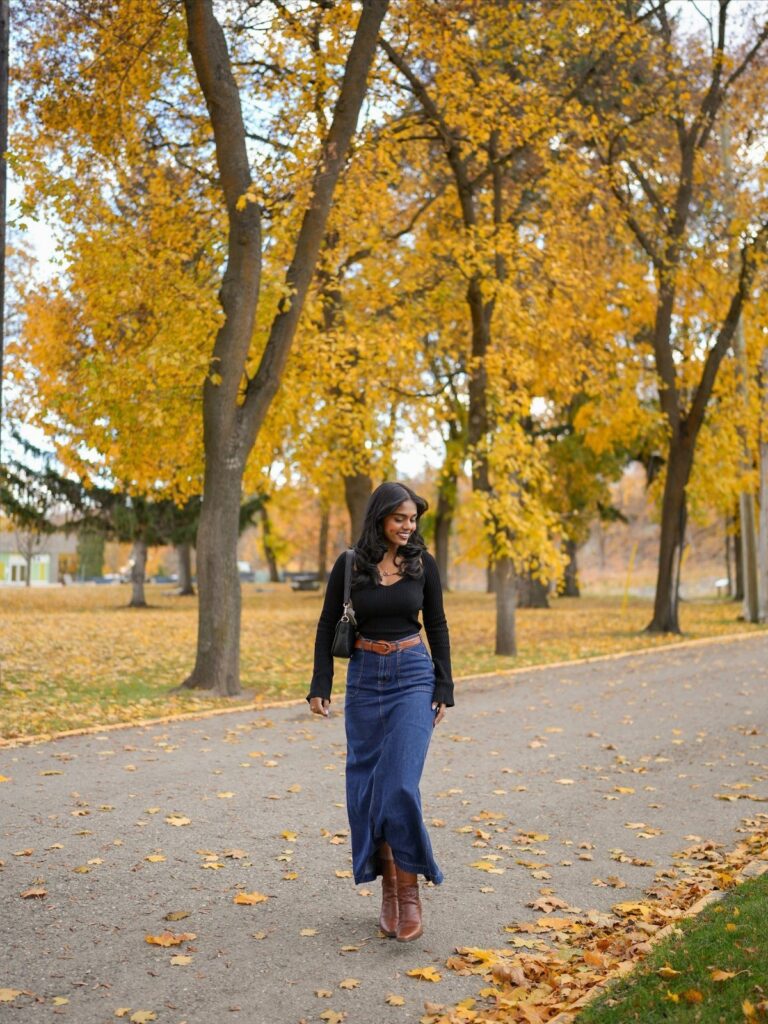 Woman wearing a blue denim midi skirt and black top in autumn park