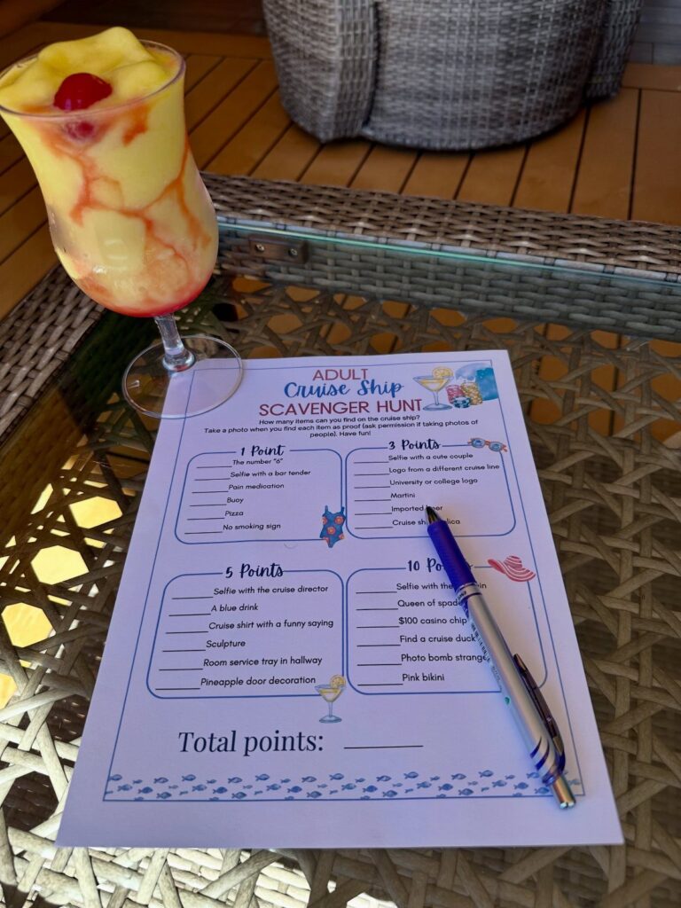 Scavenger hunt list and blue pen next to a tropical cocktail on a table.