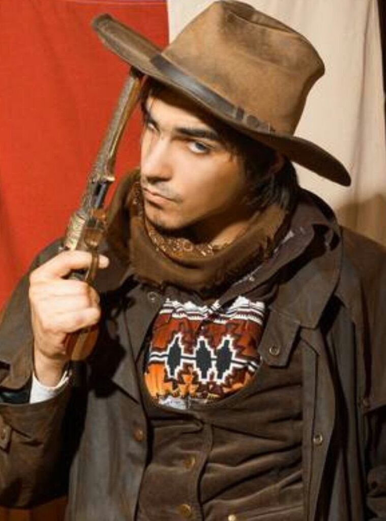 Man in brown cowboy hat and western attire holding a prop revolver