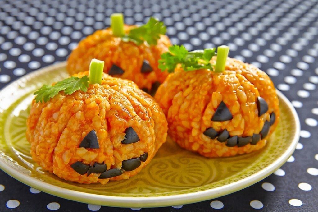 Pumpkin-shaped orange rice balls with olive faces on a yellow plate.