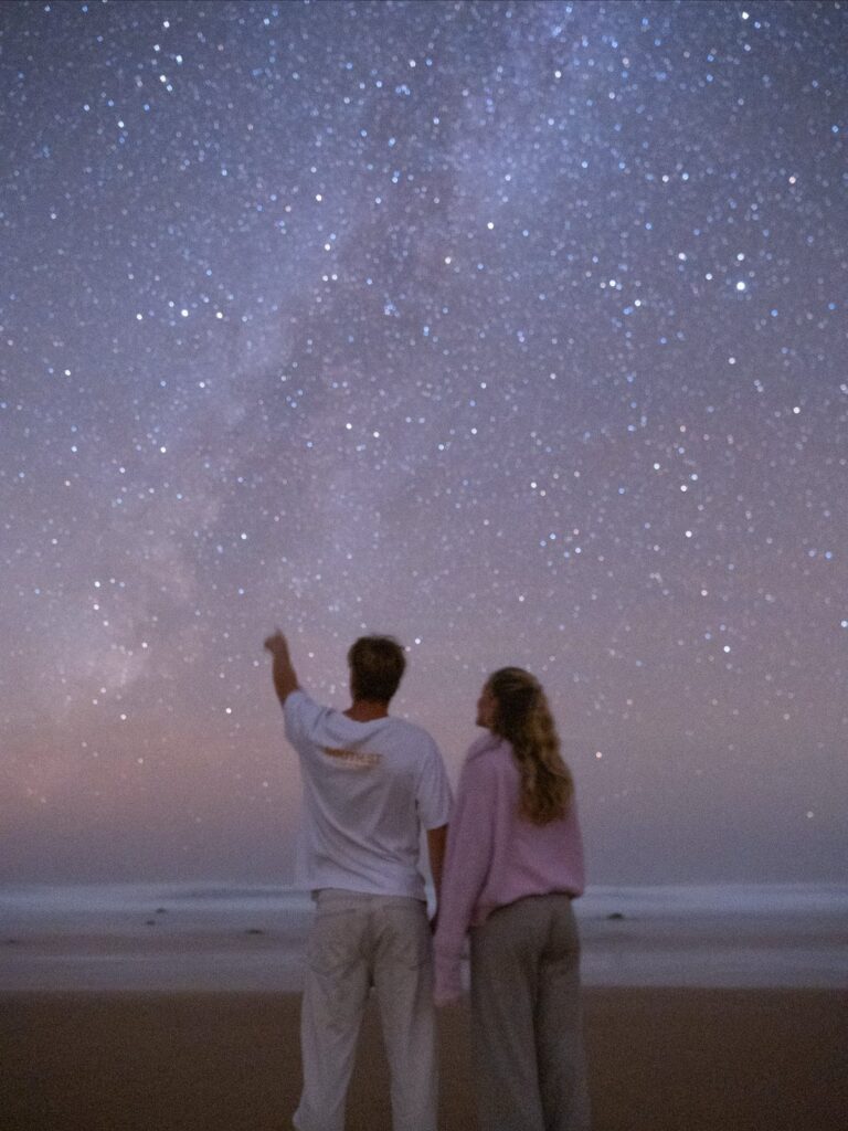 Couple standing on a beach at night looking up at a starry sky