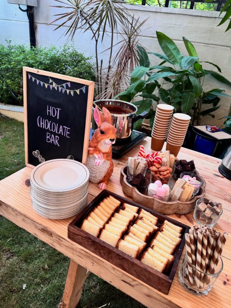 Hot chocolate bar setup on a wooden table with treats and a chalkboard sign.