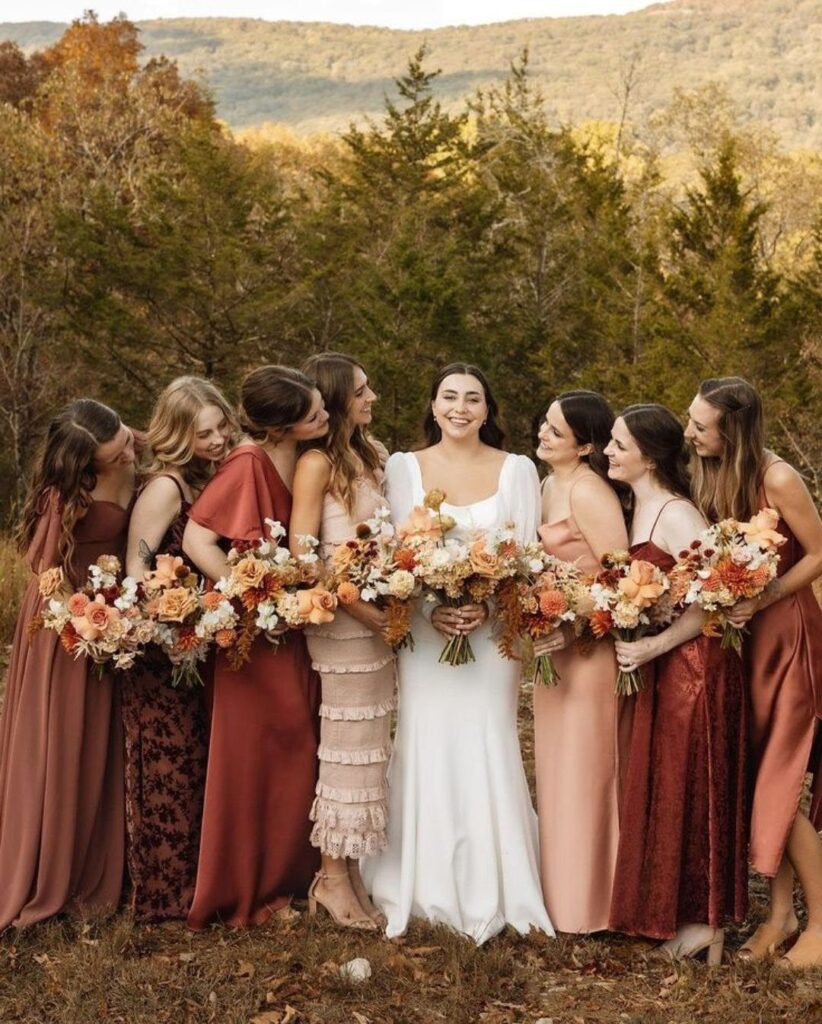 Bride and bridesmaids in autumn-toned dresses holding bouquets against a fall mountain backdrop